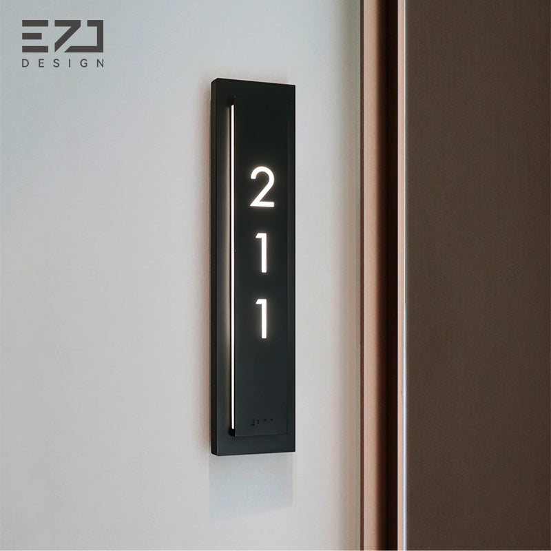 Slim black hotel room number sign shown beside a guest-room doorway