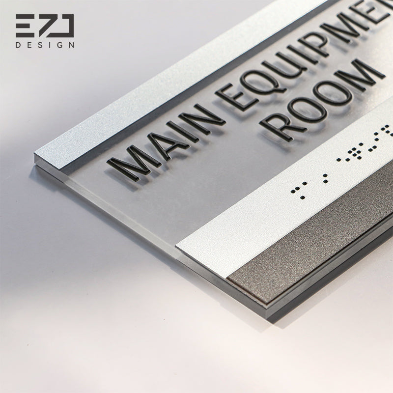 Close-up of raised tactile text and Grade 2 Braille on a silver-painted acrylic interior sign